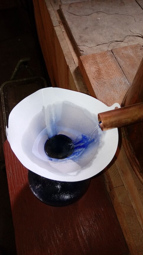 The end of the condensing pipe, emptying into the receiver, showing the clear drops of distillate turning blue.