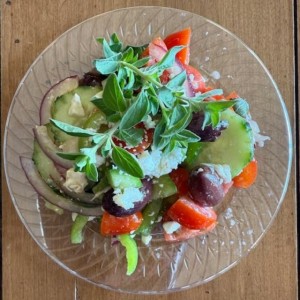 A clear plate with red onions, cherry tomatoes, olives, and an oregano sprig